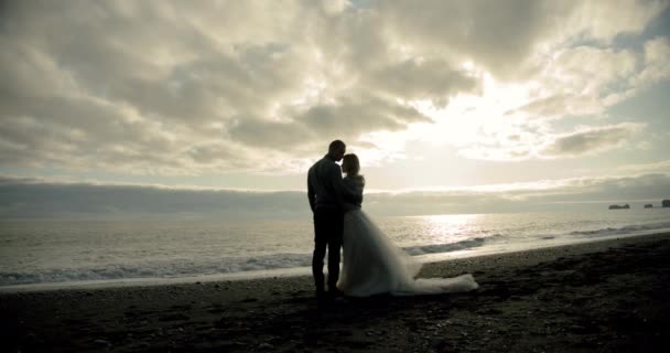 Embrasser couple de mariage se dresse contre le coucher du soleil sur une plage en Islande. — Video