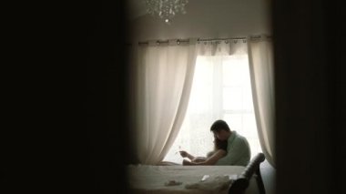 Hamile bir kadın ve kocası pencerenin önünde oturuyor ve kanepede bebeğin ultrason taramasına bakıyor. Geniş görünüm