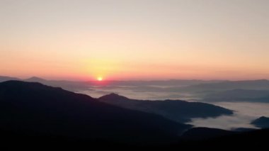 Hava aracı görüntüsü. Dağlarda gün doğumu veya gün batımı, güneşin altında ağaçların üzerinden uçmak...