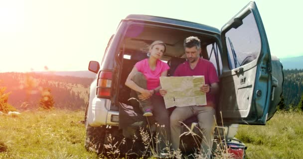 Ung man och kvinna utforska kartan sitter nära bilen i berget under solig dag. — Stockvideo
