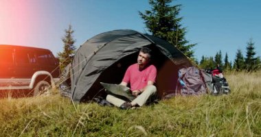 Haritayı keşfeden genç adam güneşli bir günde çadırın yanında ve arabada oturuyor..