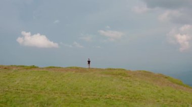 Hava aracı görüntüsü. Gün batımında dağın tepesinde uçan genç adam.
