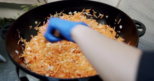 Muy cerca, las manos cocineras amasan las zanahorias en una sartén. — Vídeo de stock