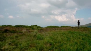Hava aracı görüntüsü. Gün batımında dağın tepesinde uçan genç adam.