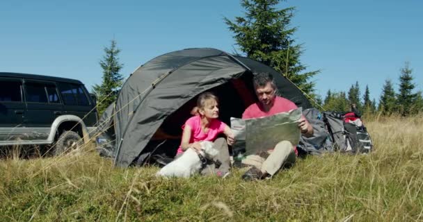 Jovem homem e mulher explorando mapa sentado perto da tenda junto com o cão e o carro na montanha durante o dia ensolarado. — Vídeo de Stock