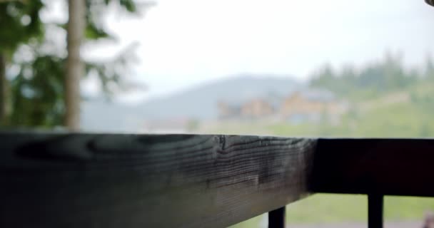 Chiudete. Mano maschile mettendo una tazza bianca su una ringhiera di legno su sfondo natura sfocata. — Video Stock