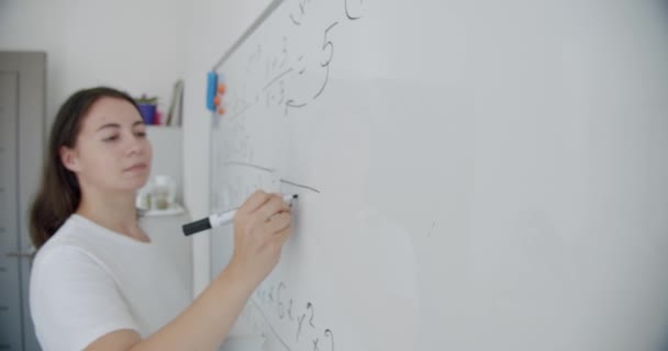 Vrouwelijke leraar schrijft op wit bord in een klaslokaal. — Stockvideo