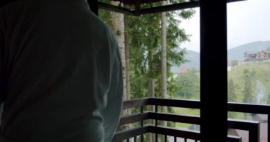 Kapatın. Beyaz bardağı beyaz bir bardağa koyan adam doğanın arka planındaki korkuluklara..