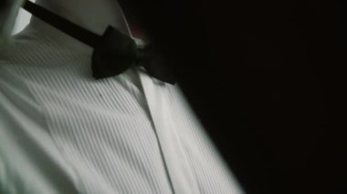 Sakallı damat beyaz gömlekli pencerenin yanında duruyor ve papyonu inceliyor..
