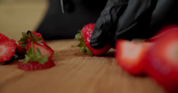 Koch in schwarzen Handschuhen schneidet frische Erdbeeren auf einem Holzschneidebrett. Nahaufnahme — Stockvideo