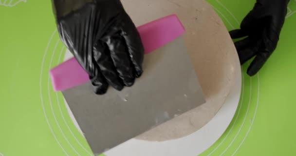 Nahaufnahme. Frau schmiert Buttercreme mit Metallspachtel in der Hand auf Kuchen. Ansicht von oben — Stockvideo