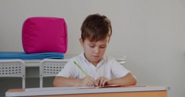 Portre okulu çocuğu masada oturuyor, ödev yapıyor, masada kağıda resim çiziyor, okulda ve evde eğitim görüyor, uzaktan eğitim alıyor..