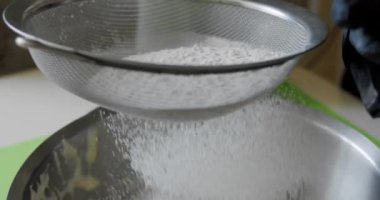 Kadın, metal kasede karıştırıcı malzemeler pişirmek için süzgeçten un geçiriyor. Yavaş çekim V3 'ü kapatın.