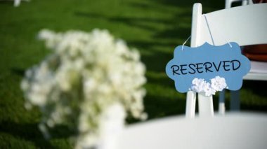 Sandalyeye bağlı küçük bir buket narin beyaz çiçekle süslenmiş, parlak mavi bir gökyüzüne kurulmuş beyaz bir tabelaya yakın plan. Yüksek kalite 4k görüntü