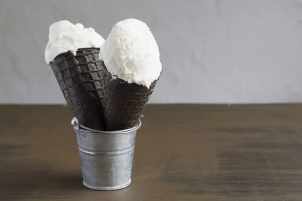 Melted ice cream in black waffle cones on a brown background.