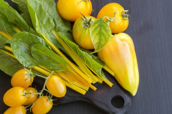 Legumes amarelos, tomates pimenta, acelga no fundo preto . — Fotografia de Stock