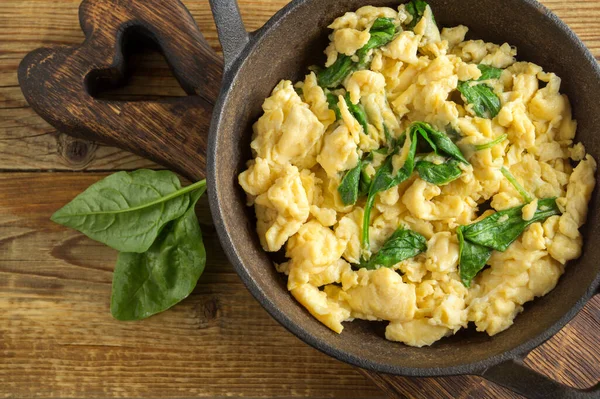 Çırpılmış yumurta ve ıspanak, dökme demir tavada. Tahta bir masada.