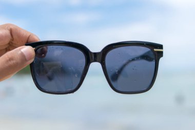 Kumsalda güneş gözlüğü tutan el