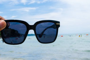 Kumsalda güneş gözlüğü tutan el