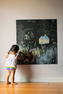 Bebek kız öğrenci bir tebeşir bir tahtaya çizer.