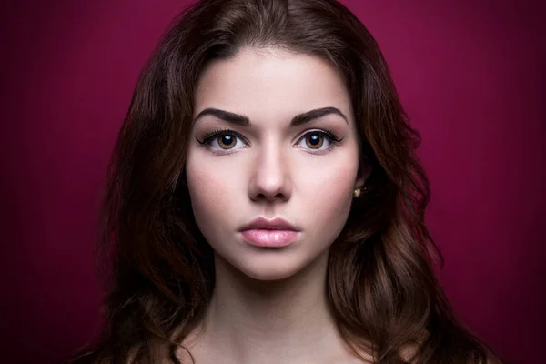 Beautiful girl looking at the camera.Shoot at studio. On a pink background. Strong face. Iris eyes. Portrait young woman. Beauty. Clean skin. Pretty model with curly hairstyle. Adult. Retouching.