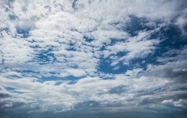 Beyaz bulutlar canlı mavi bir gökyüzünün etrafına dağılıp dinamik ve atmosferik bir manzara yaratan dairesel bir açıklık oluşturuyor.