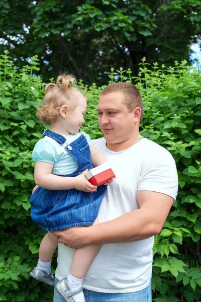 A little daughter in the arms of her father prepared to give a gift for father\'s day. A happy father on a walk with his daughter in the Park on a Sunny spring or summer day. Happy family concept