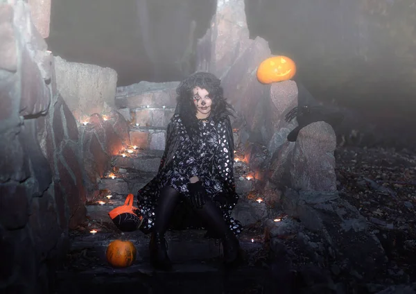 A woman with a creepy pumpkin head Jack lantern and a misty forest for Halloween. A girl with dead Princess makeup and a wreath of black roses on her head. Lit candles on the stones. Day of the dead