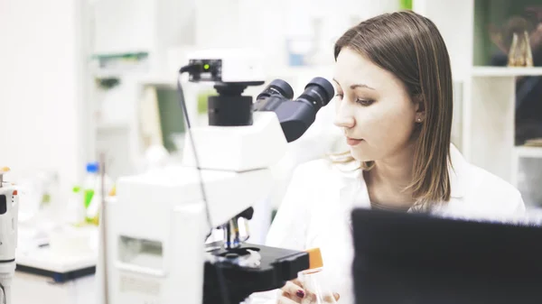 Une jeune femme médecin est assise devant le microscope — Photo