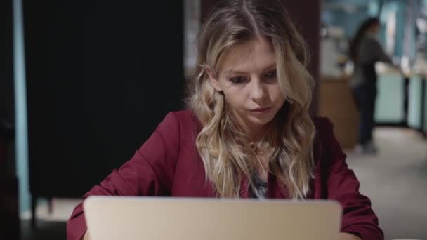 Vågig blond kaukasisk kvinna med laptop på ett café ensam — Stockvideo