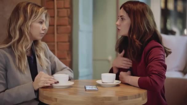 Dos mujeres jóvenes hablando en un café y mirando fotos en el teléfono inteligente — Vídeos de Stock