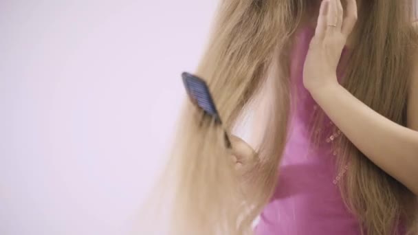 Unerkennbares kleines Mädchen in rosa, das seine langen blonden Haare kämmt — Stockvideo