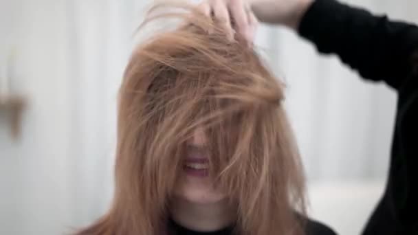 Парикмахер гладит своих молодых клиентов рыжими волосами после стрижки — стоковое видео