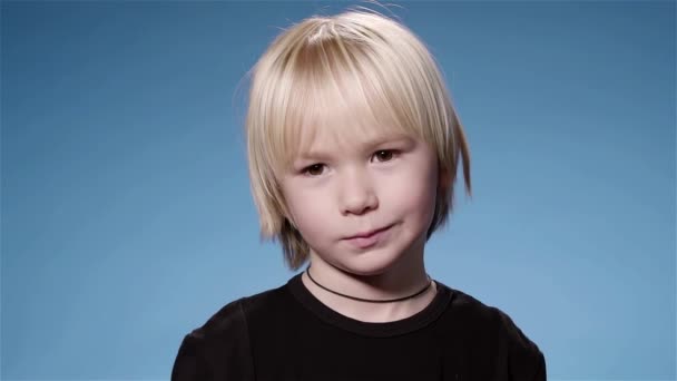 Симпатичный маленький мальчик высовывает язык, синий фон замедленной съемки — стоковое видео