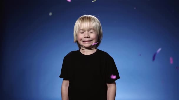 Lindo niño sorprendido por confeti y galleta, fondo azul de cámara lenta — Vídeos de Stock