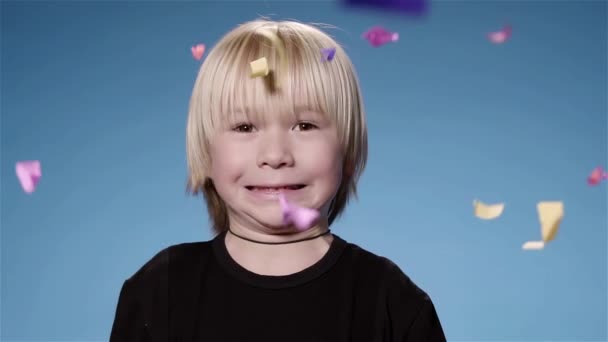 Schattige kleine jongen verrast door confetti en cracker, blauwe achtergrond super slow motion — Stockvideo