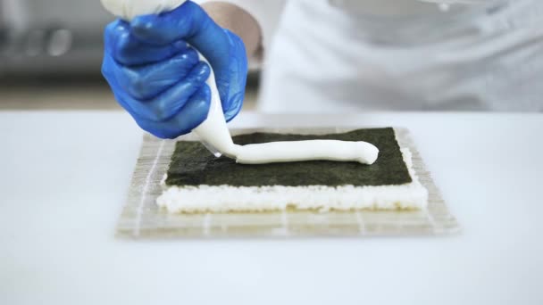 Hands of chef putting sauce and cucumber on rice making sushi — Stock Video