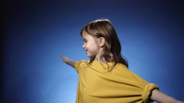 Niña sonriente en amarillo girando. Fondo azul, cámara lenta — Vídeos de Stock