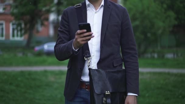 Hombre de negocios irreconocible mensajes de texto en su teléfono inteligente, ciudad borrosa verano — Vídeo de stock