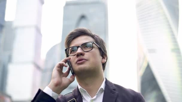 Confident young businessman talking on his phone in Moscow city, tilt up — Stock Video