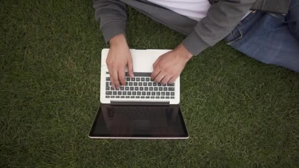 Αγνώριστος επιχειρηματίας πληκτρολογώντας σε φορητό υπολογιστή του που βρίσκεται σε έναν χορτοτάπητα, κάτοψη — Αρχείο Βίντεο