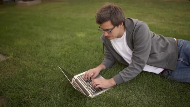 Yakışıklı işadamı bir çimenlikte, üstten görünüm yalan onun laptop yazarak — Stok video