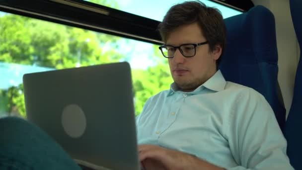 Joven hombre de negocios trabajando con el ordenador portátil en tren y sonriendo — Vídeo de stock