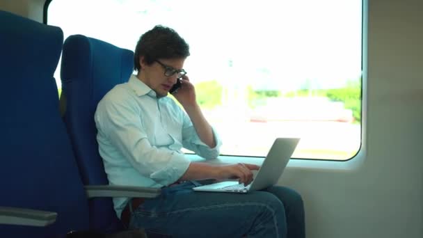 Jeune homme d'affaires parlant au téléphone et utilisant un ordinateur portable dans un train — Video