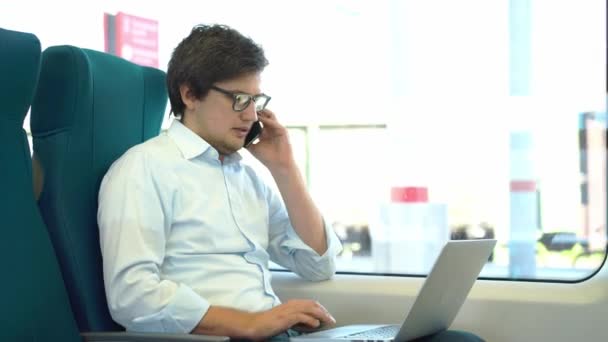Mladý podnikatel na telefonu a pomocí přenosného počítače v vlaku — Stock video