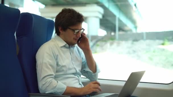 Knappe jonge zakenman op telefoon en laptop gebruikt in een trein — Stockvideo