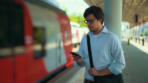 Bonito jovem empresário mensagens de texto à espera de trem na plataforma, verão — Vídeo de Stock