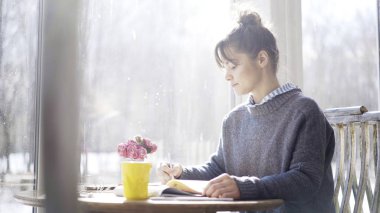 Genç esmer kız kafede bir not defterine notlar aşağı yazma