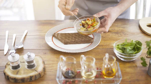 En manlig chef sätter stew sallad på en bit av en svart bröd — Stockfoto