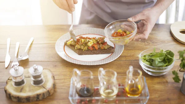 En manlig chef sätter stew sallad på en bit av en svart bröd — Stockfoto